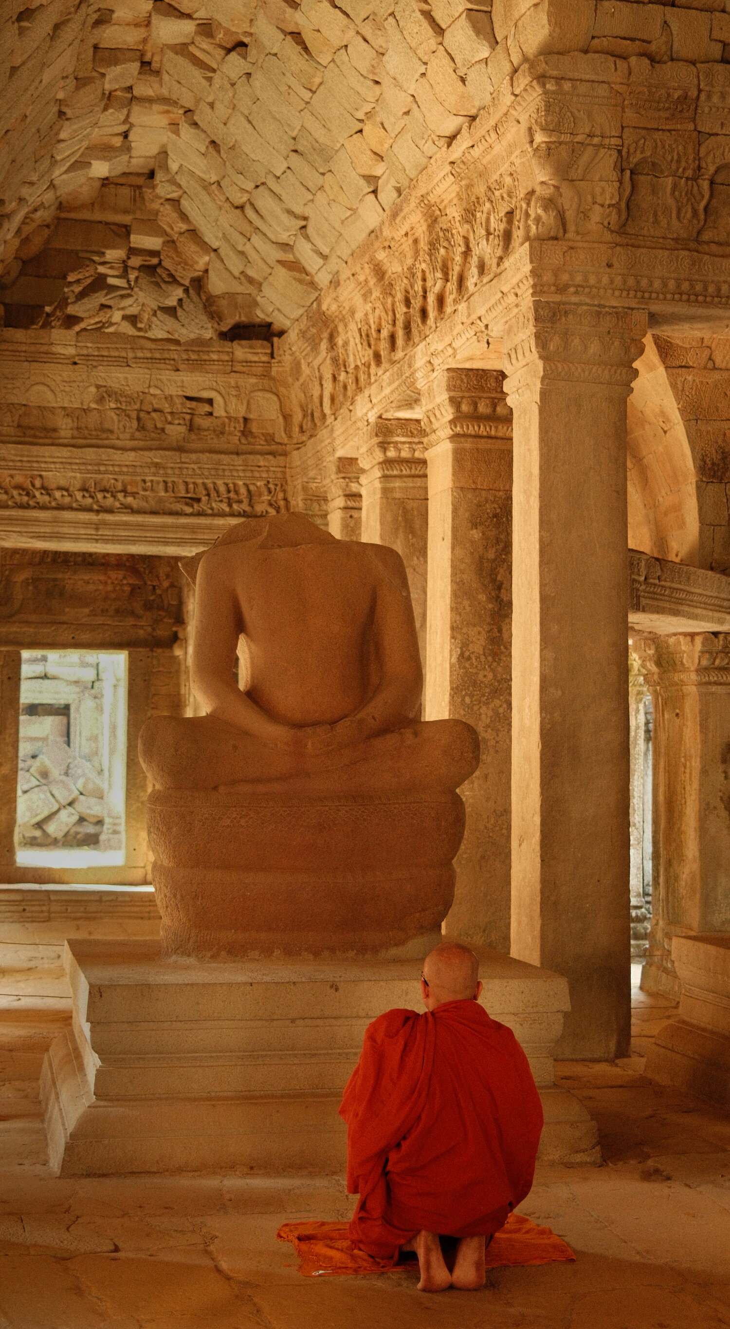 Ein Mönch vor einem kopflosen Buddha in Ta Prohm